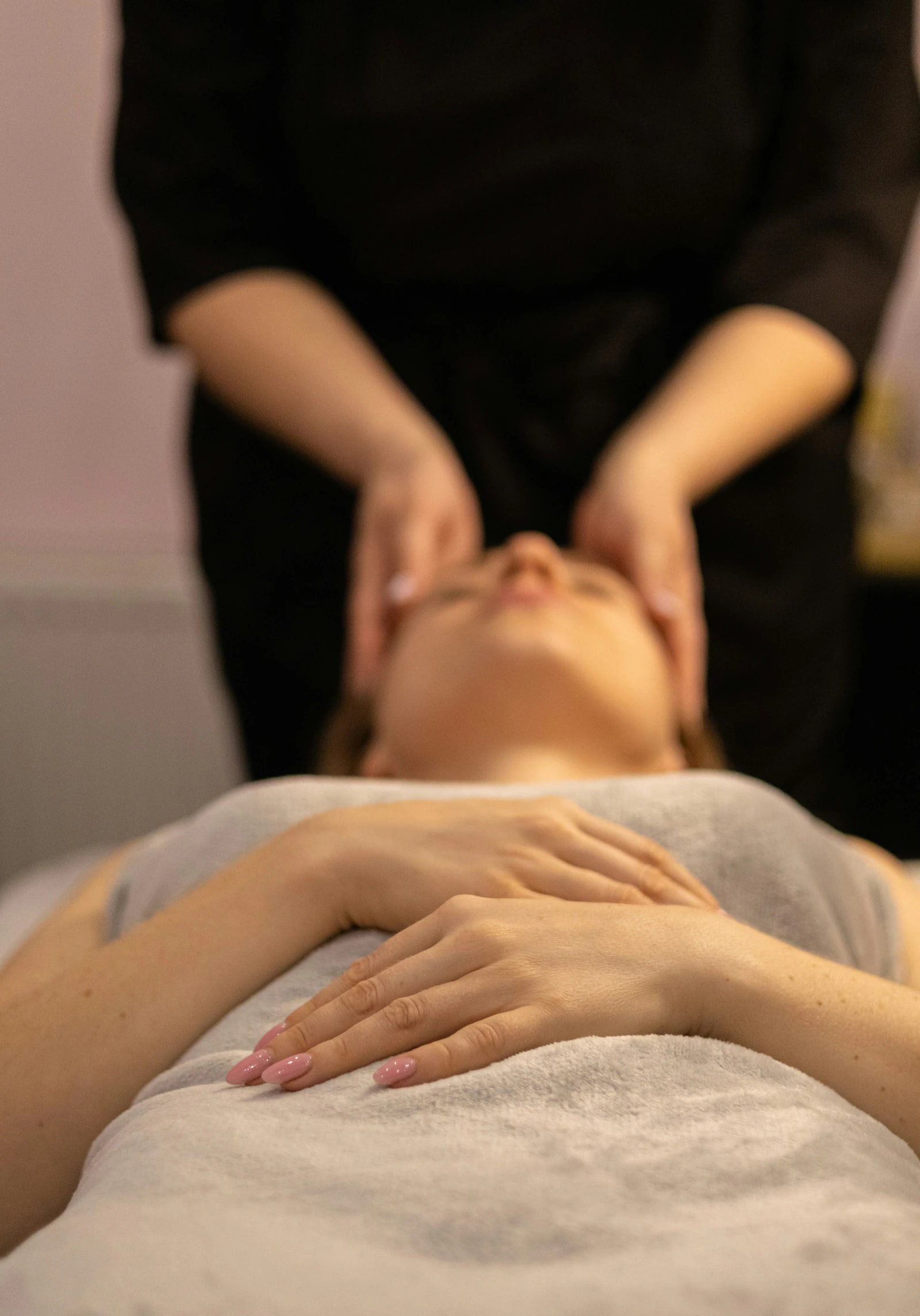 A therapist massaging a client's temples as she rests on the treatment bed