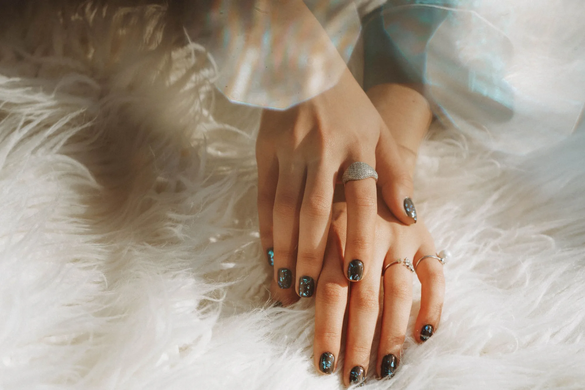 A hand with a fresh dark manicure resting on a soft white throw
