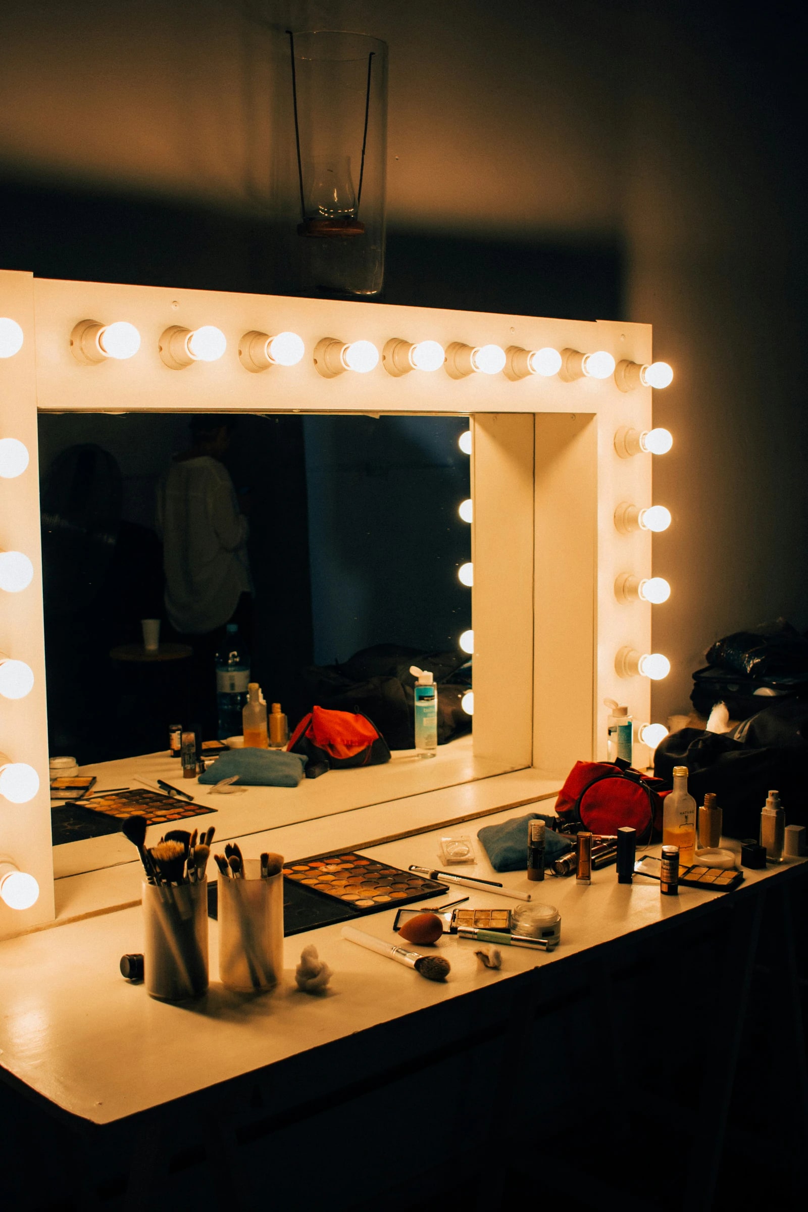 A lit makeup mirror and a table of brushes and palettes